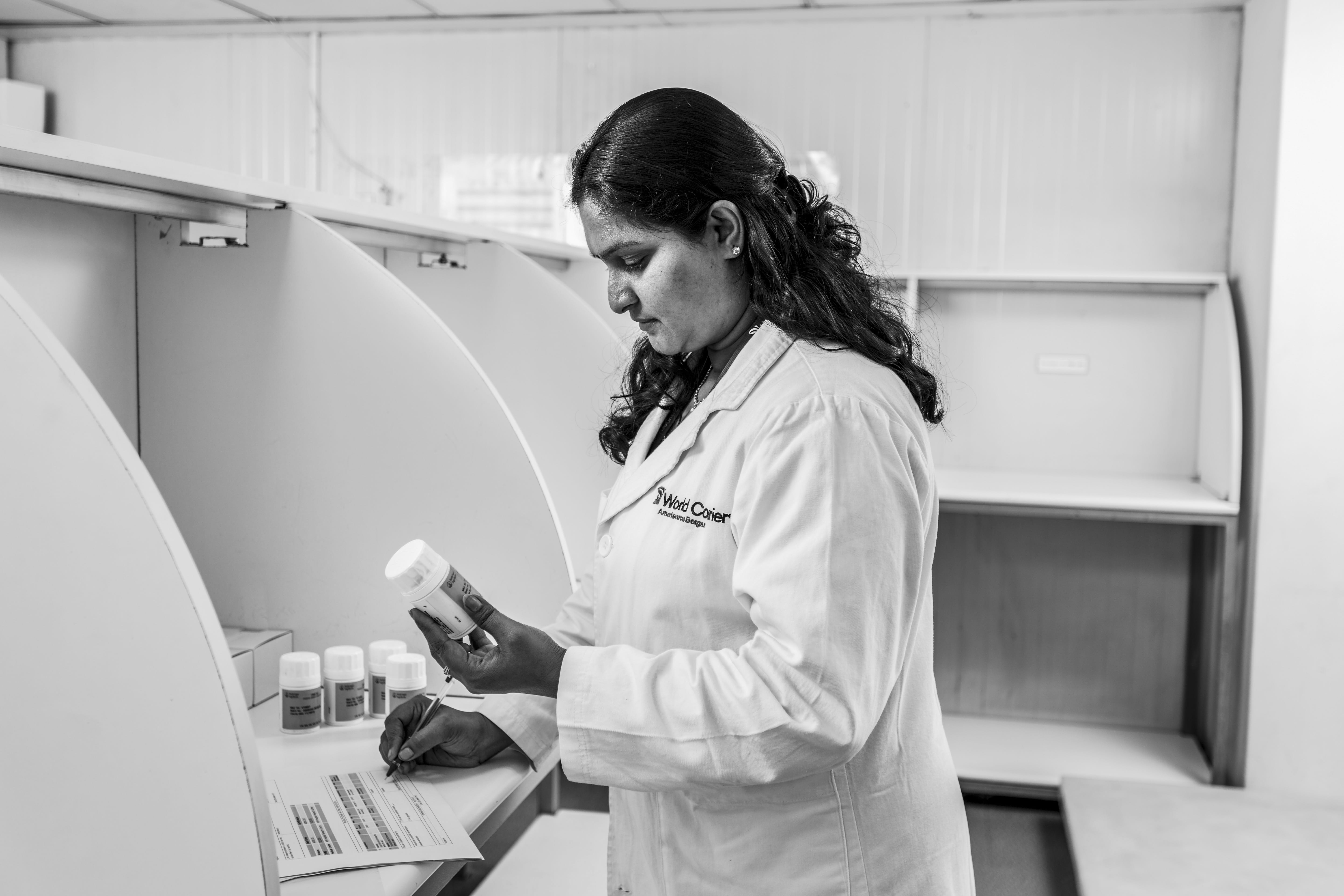 A woman in a lab coat examines a bottle of medication and takes notes.
