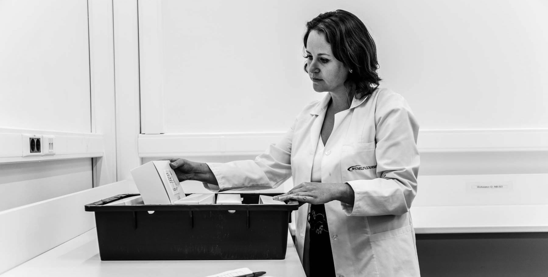 A woman in a lab coat looking at storage container with medication in it.