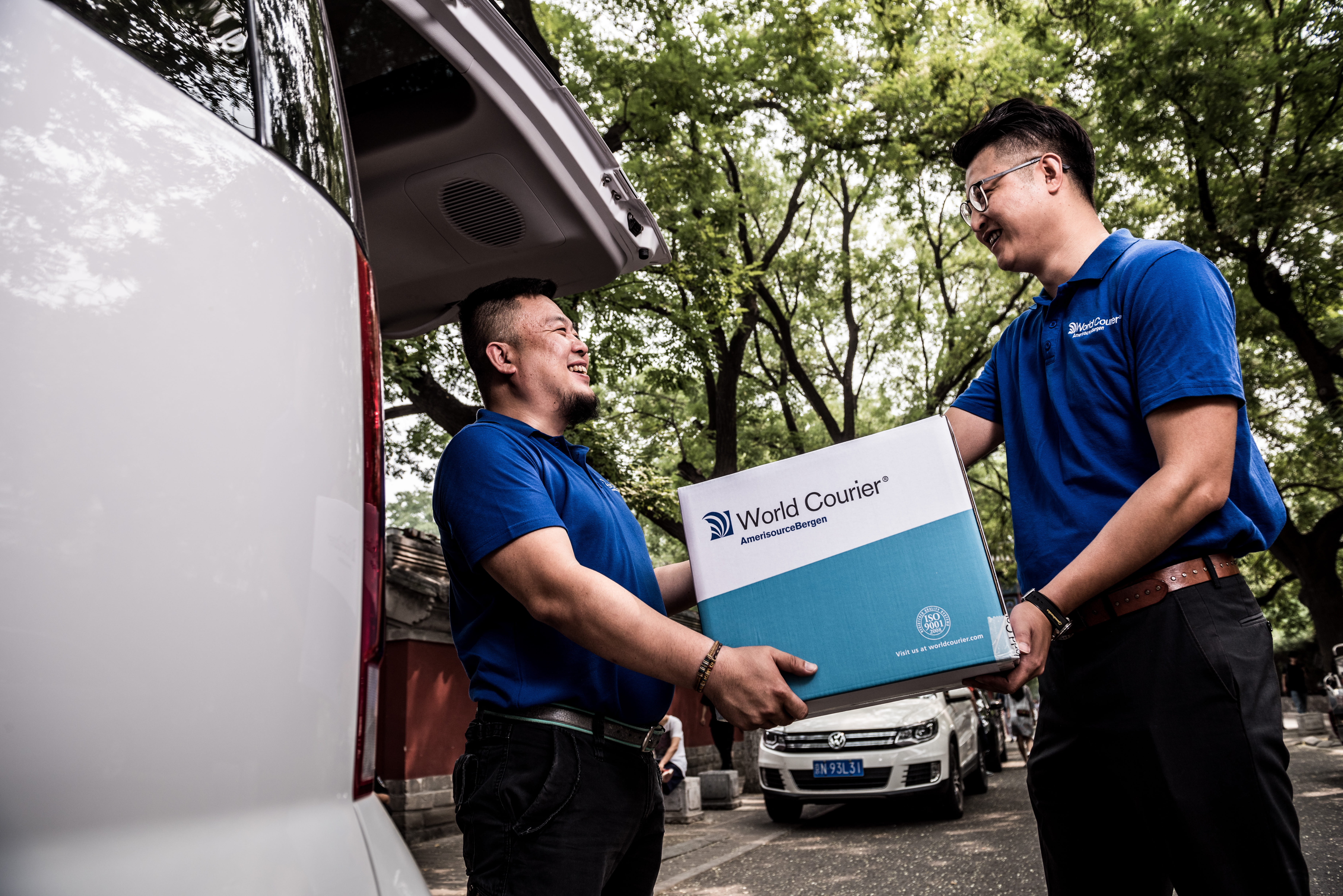 A World Courier driver passes a shipment from his van to another associate.